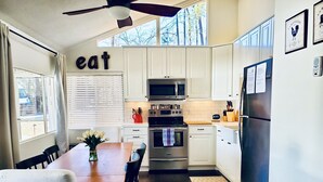 A modern kitchen with white cabinets, stainless steel appliances, and a dining area with a wooden table and chairs. - Lake Front Getaway, Family Friendly. (Mooresville)