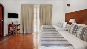 Una habitación de hotel con cama, sofá, televisor, escritorio y cortinas.
