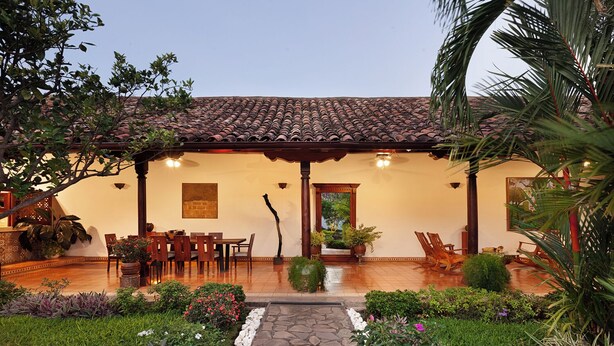 Un edificio tradicional con techo de tejas, un patio con muebles de madera y un jardín con diversas plantas y flores.