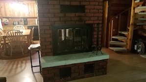 A cozy living room with a brick fireplace, wooden furniture, and a staircase.