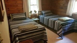 Ein Blockhauszimmer mit zwei Betten, Holzwänden und einem Fenster mit Vorhängen.