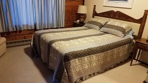 A bedroom with a large bed, a nightstand, a lamp, and a window with curtains.