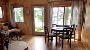 A wooden interior with a dining table and chairs, a clock on the wall, and large windows with curtains. - Cozy Lake Front Cabins For A Wonderful Summer, Fall and Winter fun Get Away!
 (Emily)