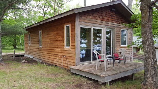 A wooden cabin with a deck, large windows, and a covered porch with chairs. - Cozy Lake Front Cabins For A Wonderful Summer, Fall and Winter fun Get Away!
 (Emily)