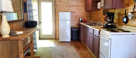 Una cocina compacta con paredes de madera, un refrigerador, una estufa y un lavamanos.