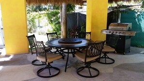 Eine Terrass mit rundem Tisch und Stühlen, einem Grill und einem Reetdach.