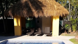 Eine strohgedeckte Hütte mit einem Pool davor.