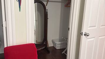 A room with a red chair, a wooden floor, a white door, a mirror, a laundry basket, and a hanging coat rack.