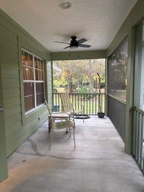 A covered porch with a ceiling fan, two chairs, a potted plant, and a view of a yard with trees and a fence. - Hobe Sound Natural Setting. New lightning fast internet. Great seclusion! (Hobe Sound)