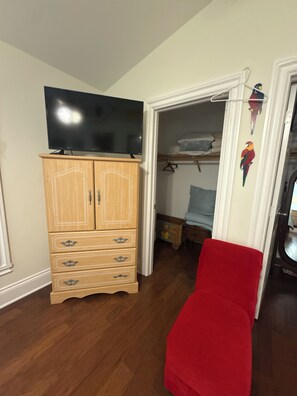 A room with a wooden cabinet, a flat-screen TV, a red chair, and a closet with hanging clothes. - Hobe Sound Natural Setting. New lightning fast internet. Great seclusion! (Hobe Sound)