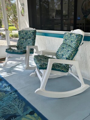 A porch with three rocking chairs, a white railing, and a blue patterned rug.
