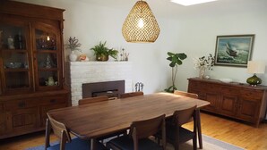 Zona pranzo con tavolo e sedie in legno, camino, mobile con vetrine e lampadario.