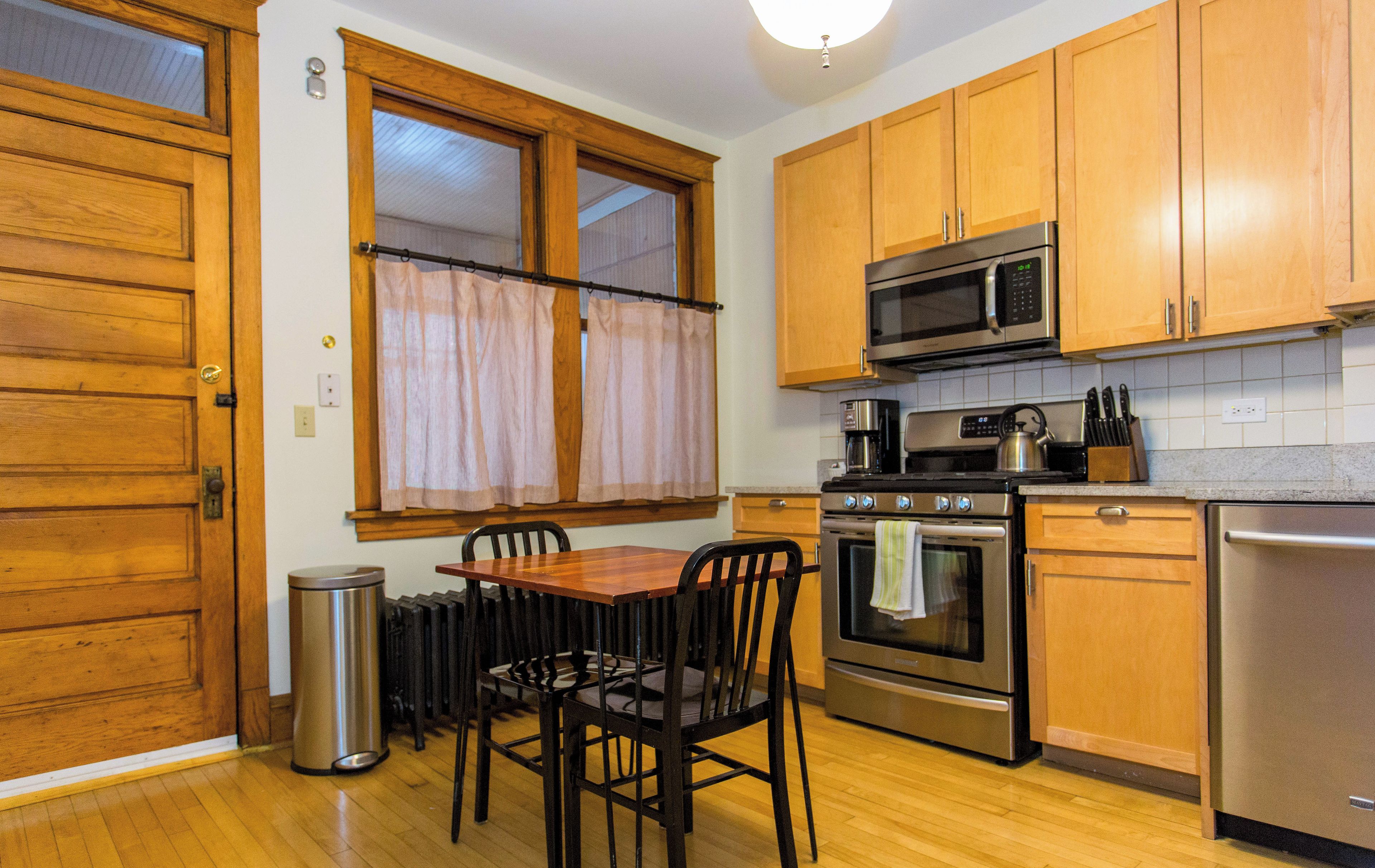 Una cocina con armarios de madera, un refrigerador de acero inoxidable, un horno, un microondas y una mesa de comedor con sillas.