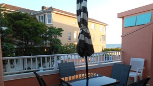 A balcony with a table and chairs, an umbrella, and a view of a building and trees. - Coquina Beach Club 110, Beachfront Studio. Booking late summer weeks. (Bradenton Beach)