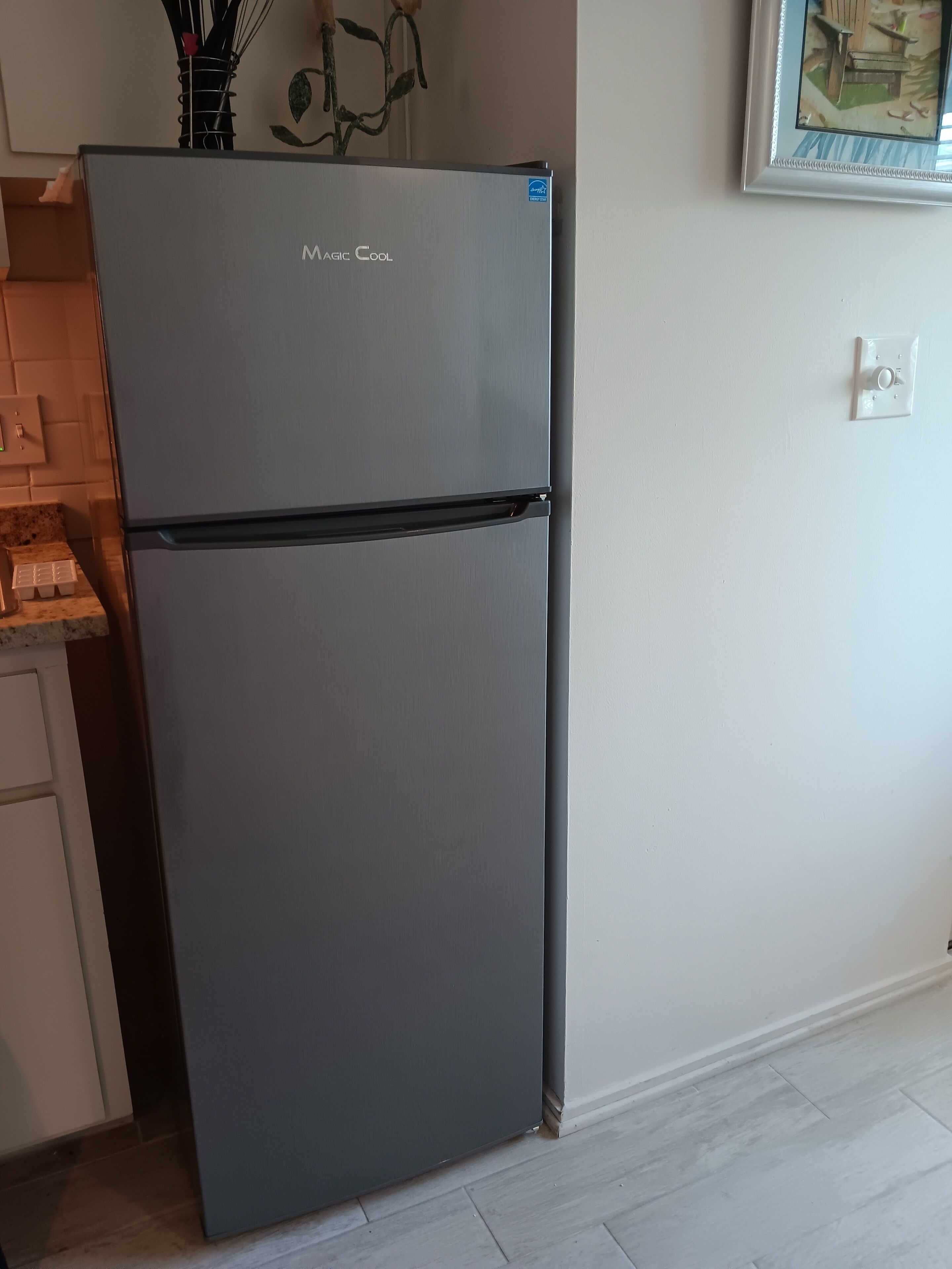 Una cocina moderna con un refrigerador gris, una pequeña encimera e interruptor de luz en la pared.