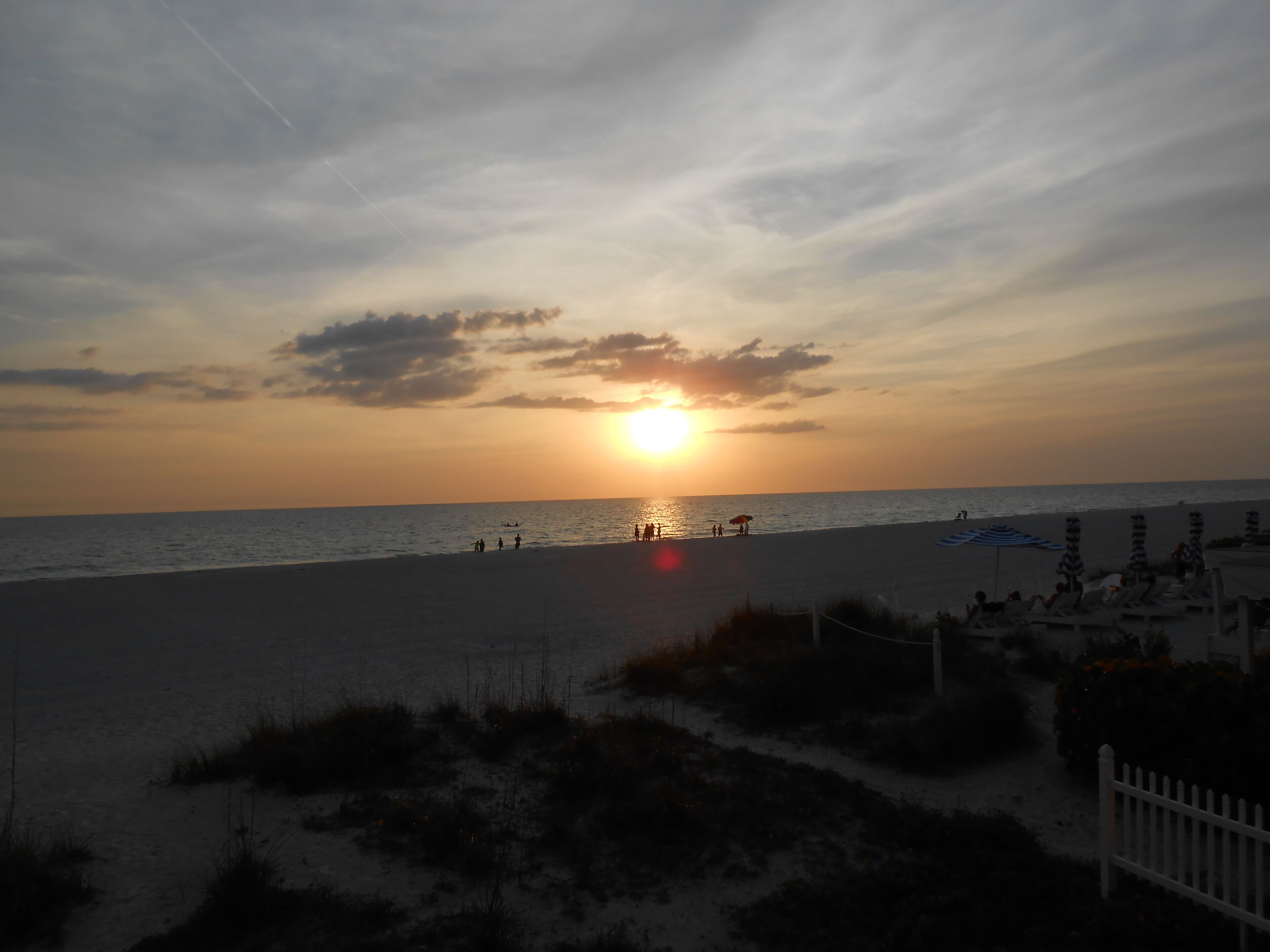 A beach with a sunset, umbrellas, and lounge chairs.