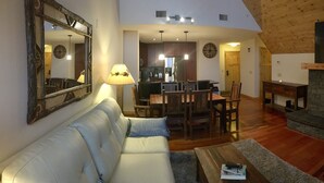 A living room with a fireplace, a sofa, a dining area, and a kitchen in the background. - Premium penthouse in the heart of the Canadian Rockies! Walk to busy downtown. (Canmore)