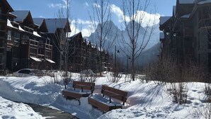 A snow-covered outdoor area with wooden benches, a car, and buildings with wooden facades and snow on the roofs. - Premium penthouse in the heart of the Canadian Rockies! Walk to busy downtown. (Canmore)