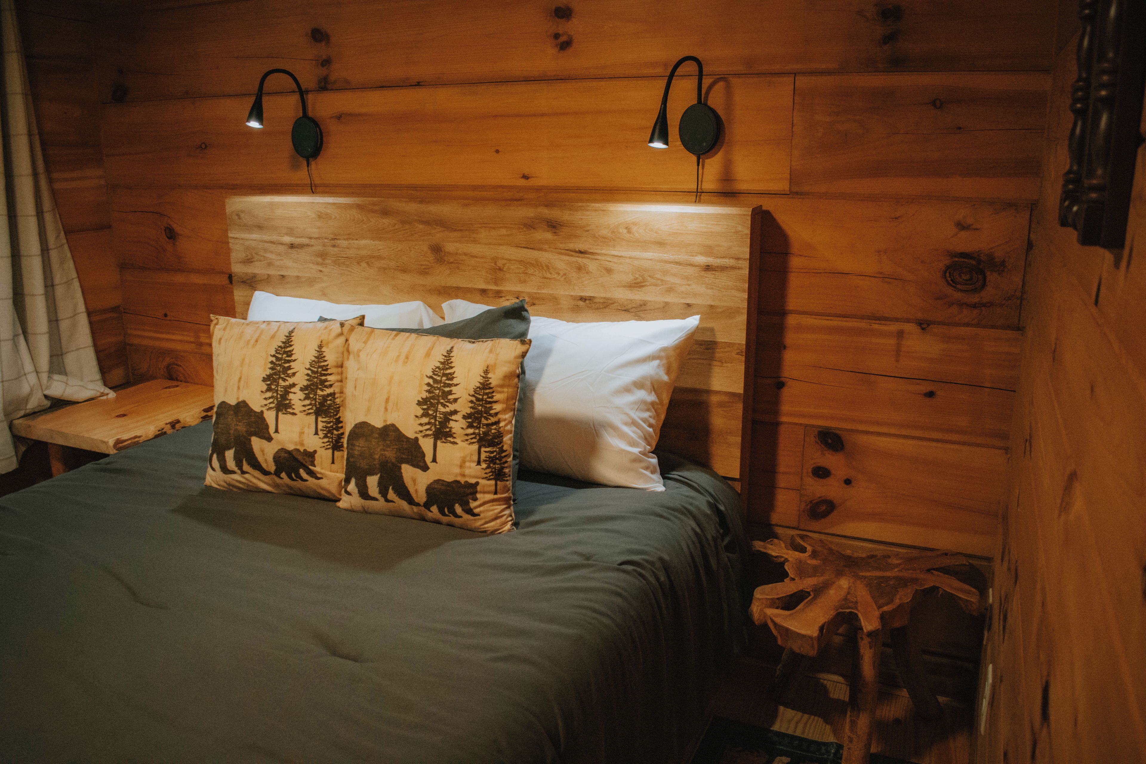 Ein Zimmer in einer Holzhütte mit einem Bett, zwei Wandlampen und einem Kopfkissen mit Bär-Motiv.