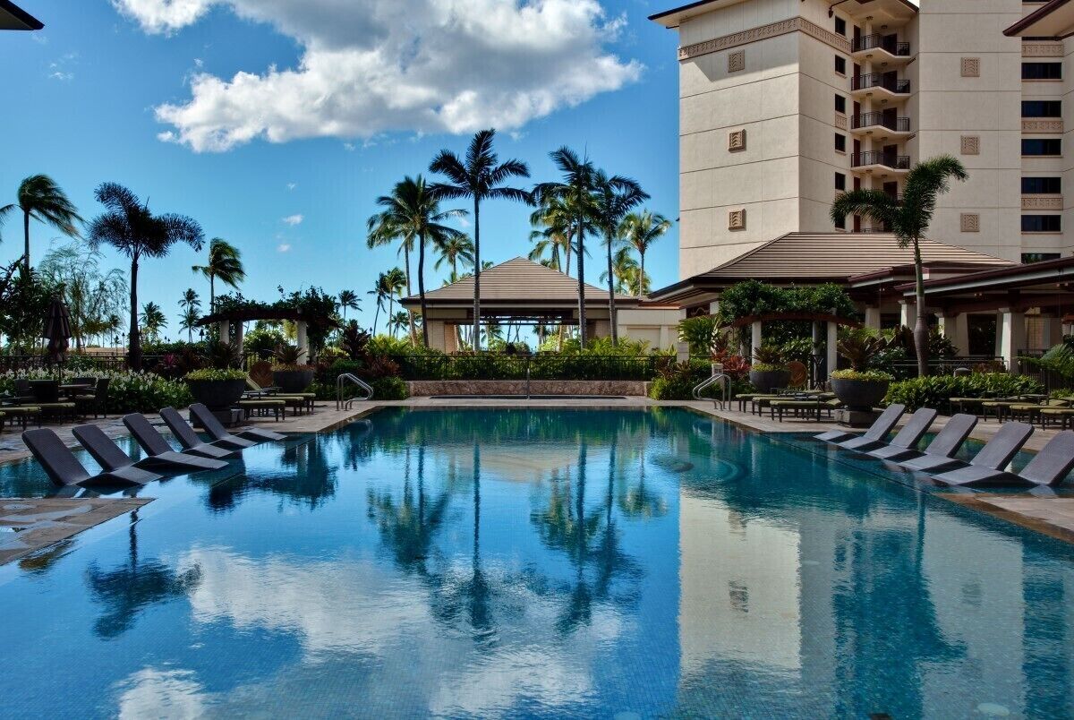 A swimming pool with lounge chairs, palm trees, and a building with balconies.