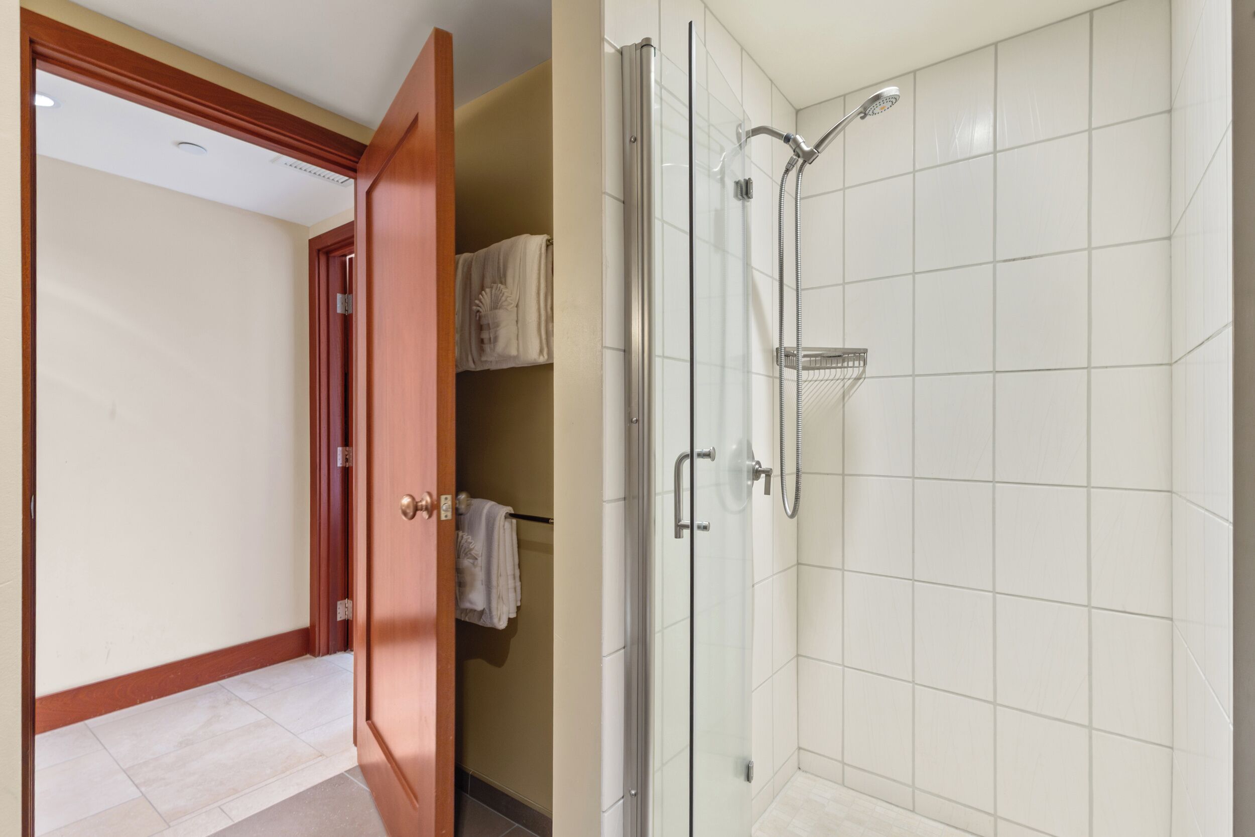 A bathroom with a glass shower enclosure, a towel rack, and a door leading to a hallway.