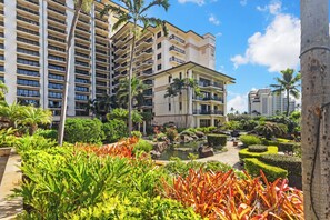A multi-story hotel with balconies, a landscaped garden with various plants, and a small pond. - Ko Olina Luxury beachfront condo next to Disney Aulani and Marriott's Beach Club (Kapolei)