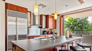 Una cocina moderna con una isla central, electrodomésticos de acero inoxidable, armarios de madera y un amplio ventanal con vistas al verdor.
