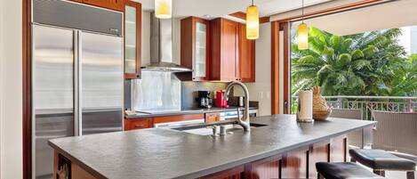 Una cocina moderna con una isla central, electrodomésticos de acero inoxidable, armarios de madera y un amplio ventanal con vistas al verdor.