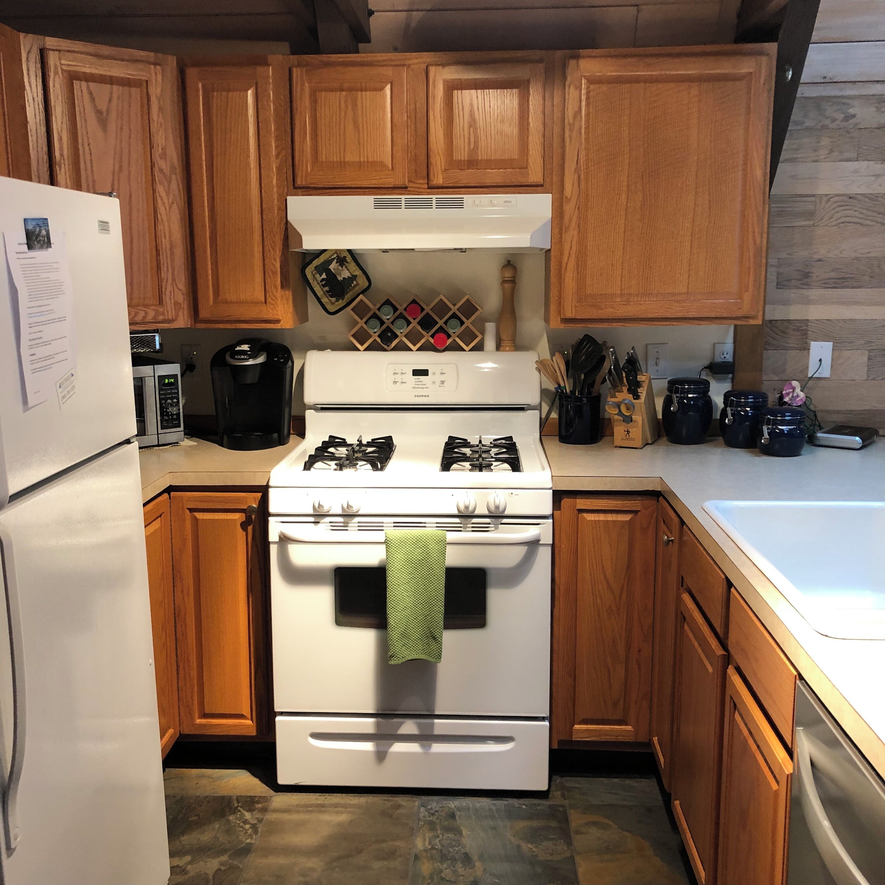 Una cocina con armarios de madera, una estufa blanca, un refrigerador y una cafetera.
