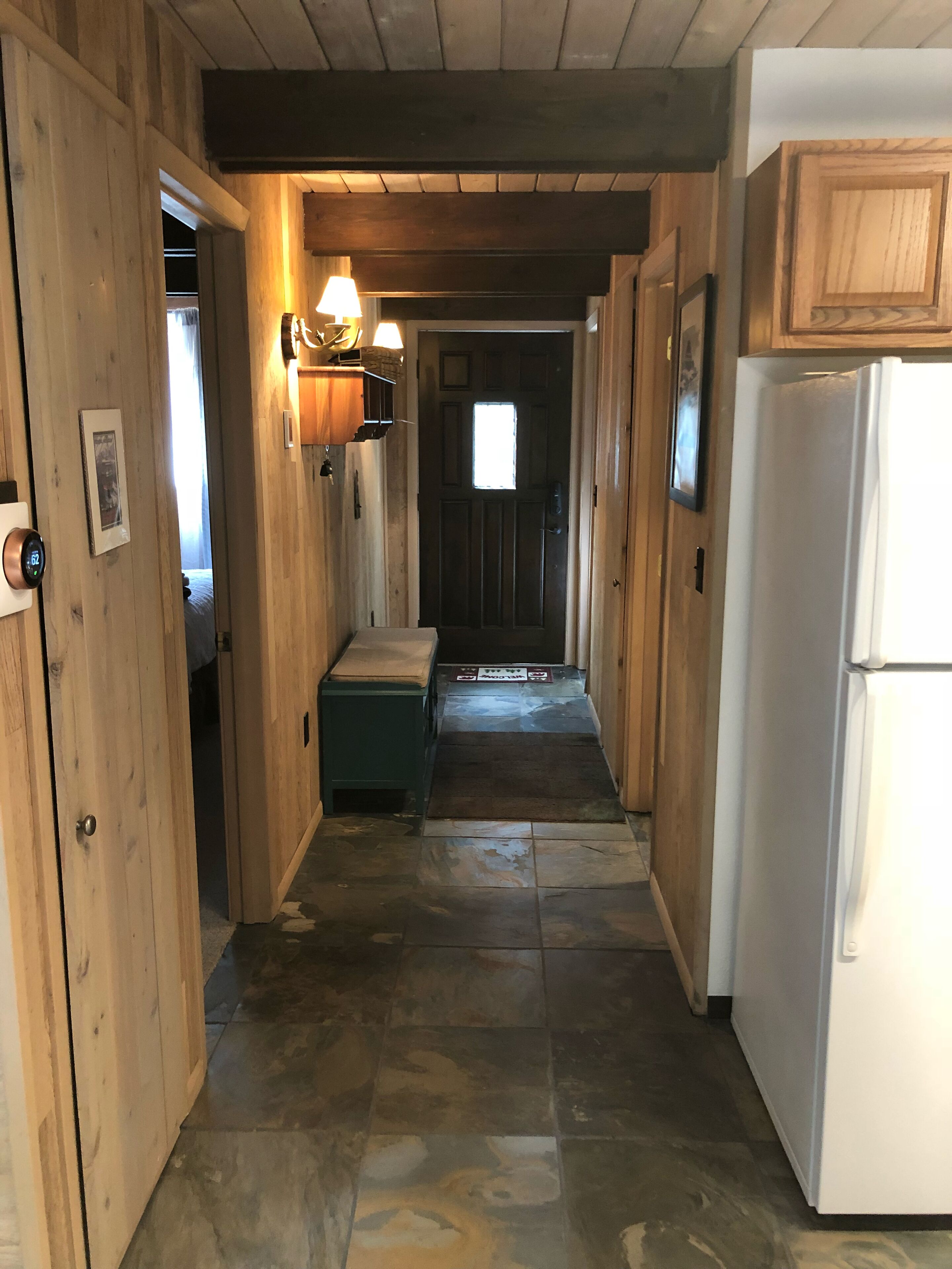 Un couloir intérieur aux murs en bois, avec un réfrigérateur, un banc et une porte donnant sur une autre pièce.