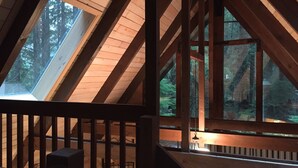 Ein Dachzimmer mit Holzbalken, Dachfenstern und Blick auf einen Wald.