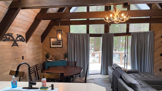 Ein gemütliches Blockhaus-Interieur mit einem Essbereich aus Holz, einer modernen Küche mit Spüle und einer Sitzecke mit Sofa und Bank.