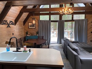 L’intérieur chaleureux d’un chalet comprend un coin repas en bois, une cuisine moderne avec un évier et un espace salon avec un canapé et un banc.