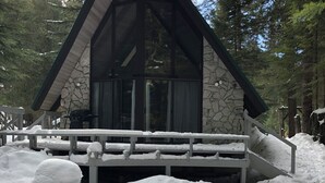 Eine Holzhütte mit Steinverkleidung und einem steilen Dach, umgeben von Schnee und Bäumen.