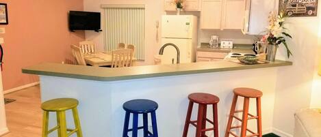 A compact kitchen with a central island, a dining area, and a bar stool arrangement.