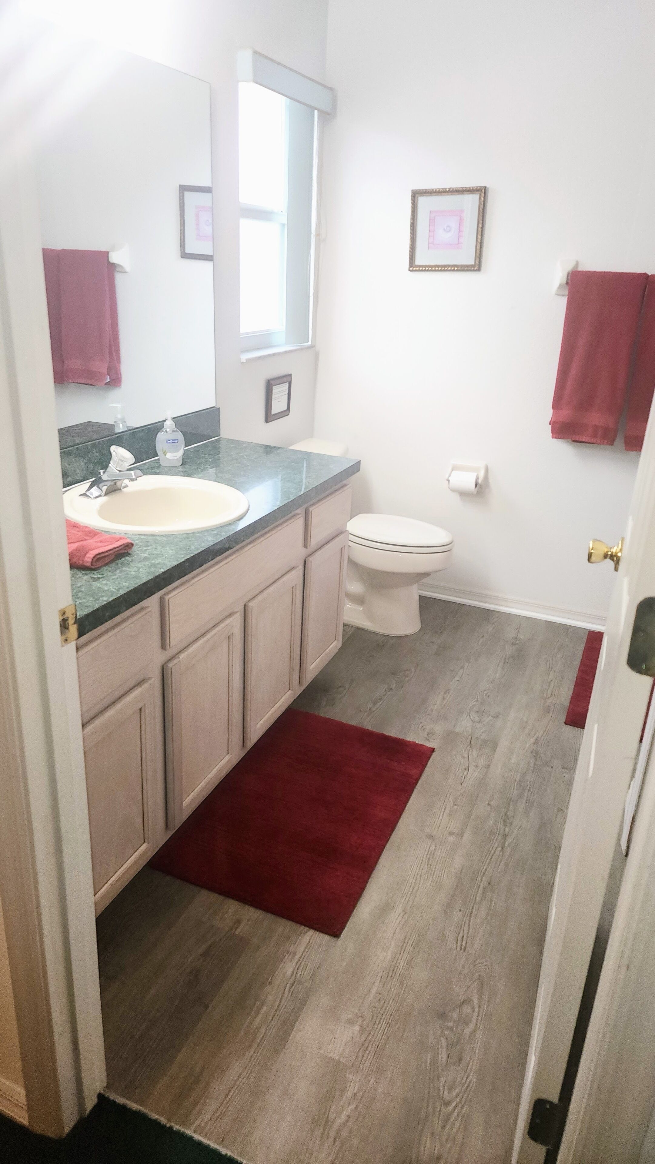 A bathroom with a sink, mirror, toilet, and a red rug.