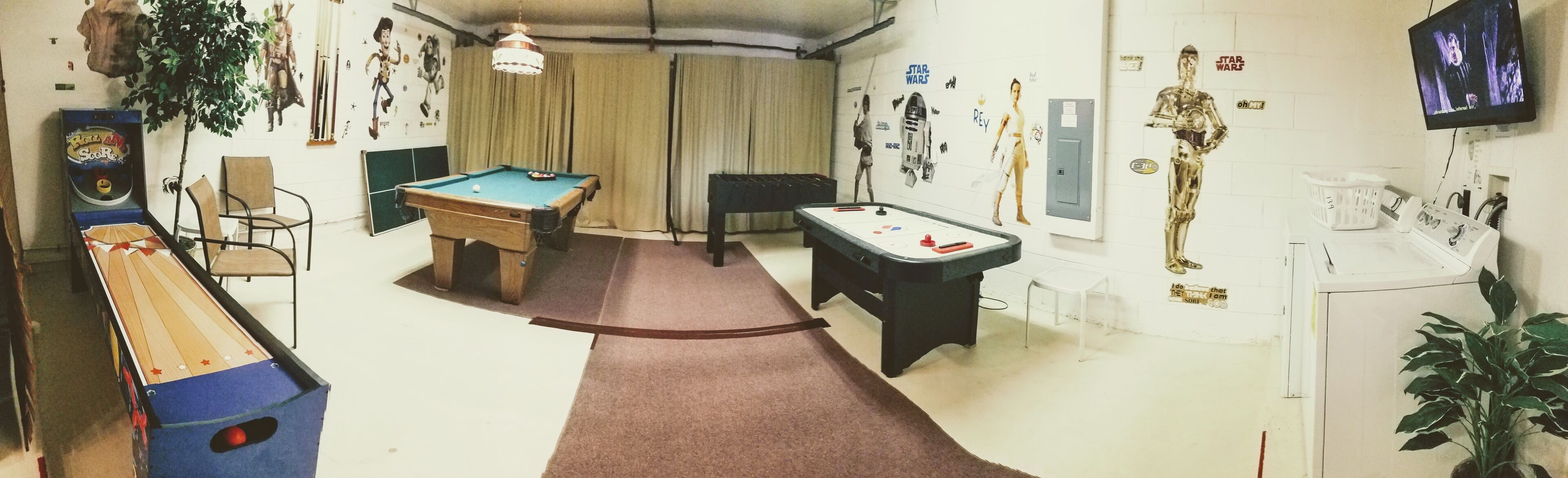 A room with a pool table, a foosball table, and a Star Wars-themed wall.