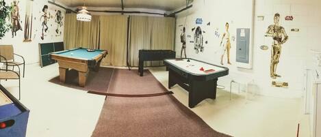 A room with a pool table, a foosball table, and a Star Wars-themed wall.