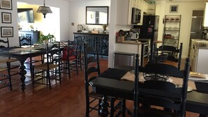 A spacious dining area with a wooden table and chairs, a kitchen in the background, and a large mirror above the table.