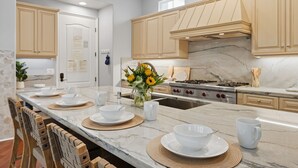 Cocina moderna con encimeras de mármol, armarios de madera y una isla central con pileta y un florero de girasoles.
