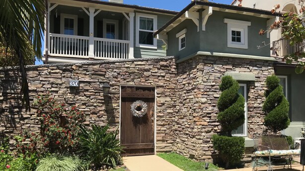 Una casa de piedra con porche, una puerta principal adornada con un adorno y un pequeño patio con una silla.