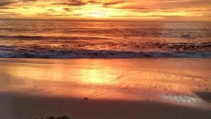 Una playa con huellas y un corazón dibujado en la arena, reflejando el atardecer.