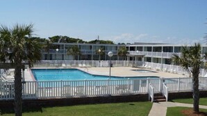 A pool area with a white fence, palm trees, and a building with multiple balconies in the background. - Come for the beach, stay for the memories. Enjoy free beach access & huge pool! (Atlantic Beach)