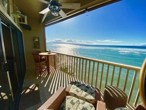 Ein Balkon mit Meerblick, Holzmöbel und einem Deckenventilator.