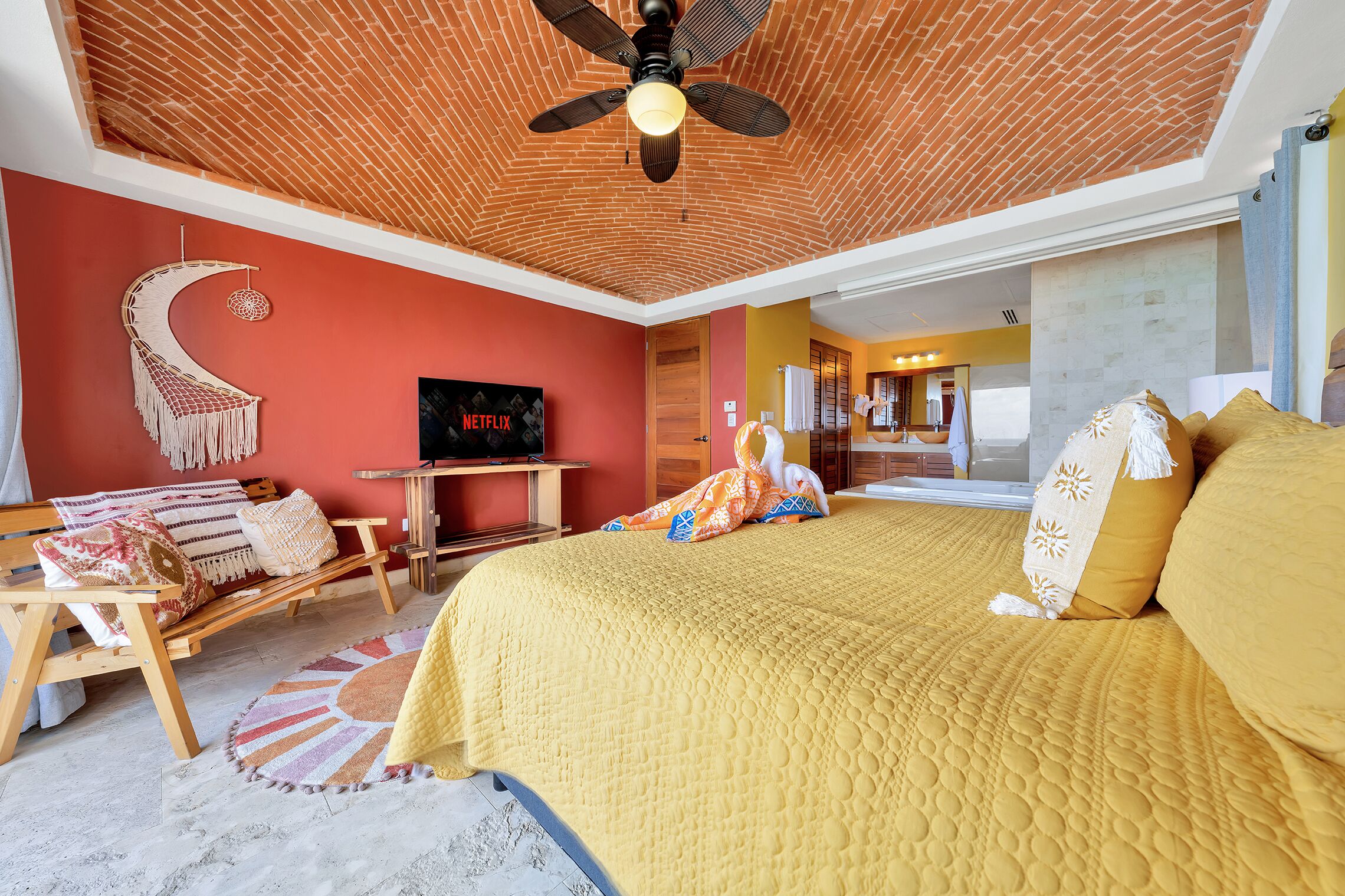 A room with a bed, a desk, a chair, a macrame wall hanging, and a ceiling fan.