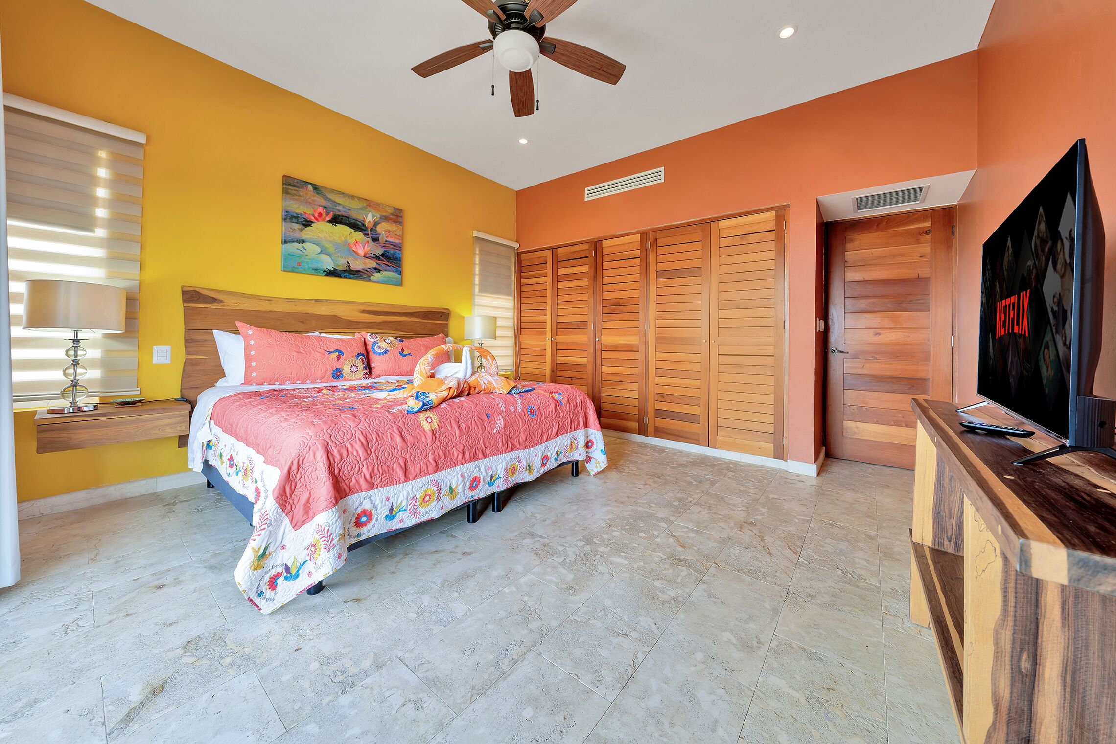 A bedroom with a bed, a ceiling fan, a TV, and wooden closets.