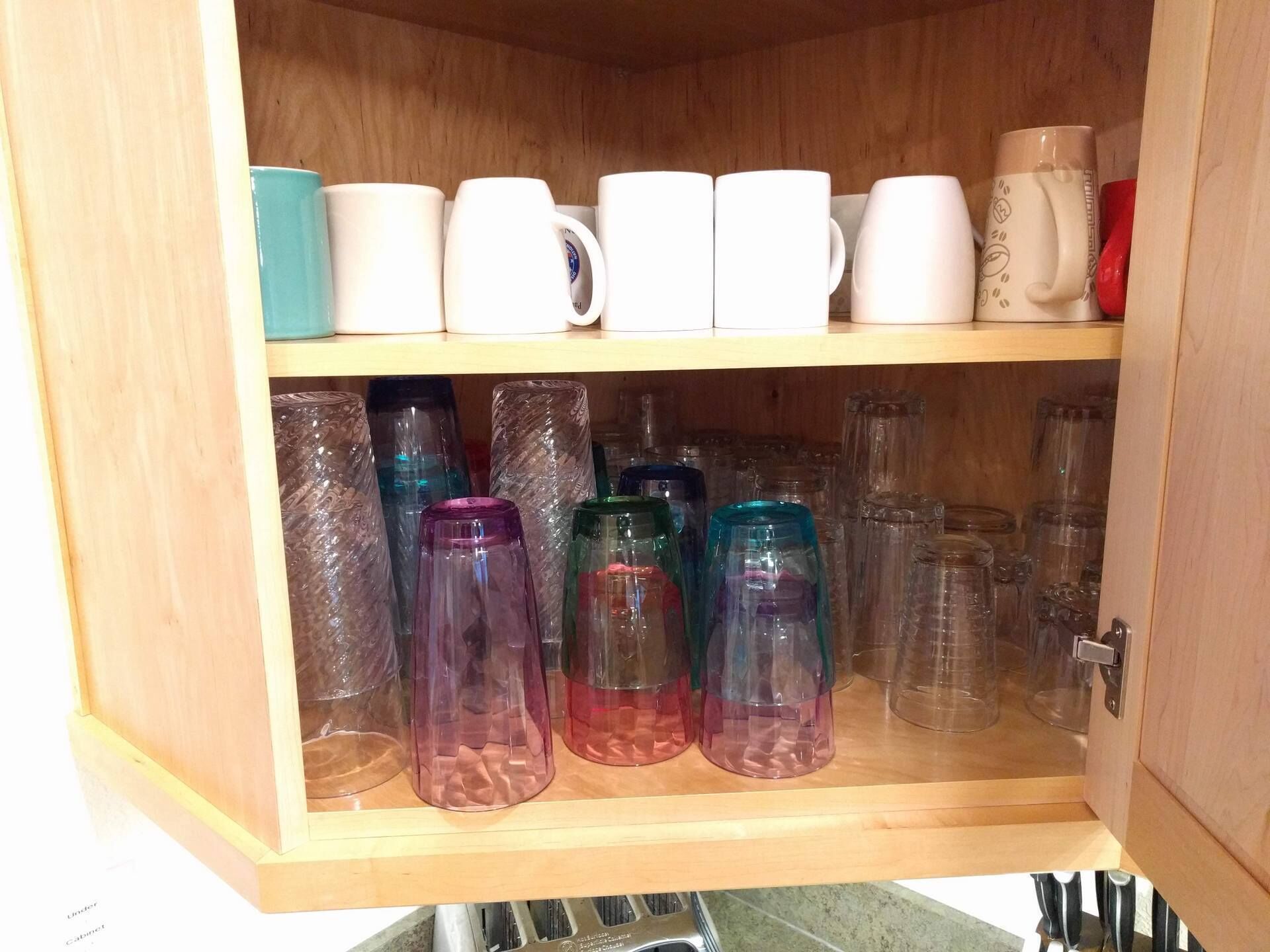 A wooden cabinet with shelves holding various glass containers and mugs.