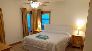 Ein Schlafzimmer mit einem Bett, zwei Nachttischen, einem Deckenventilator und Blick ins Freie durch zwei Fenster.