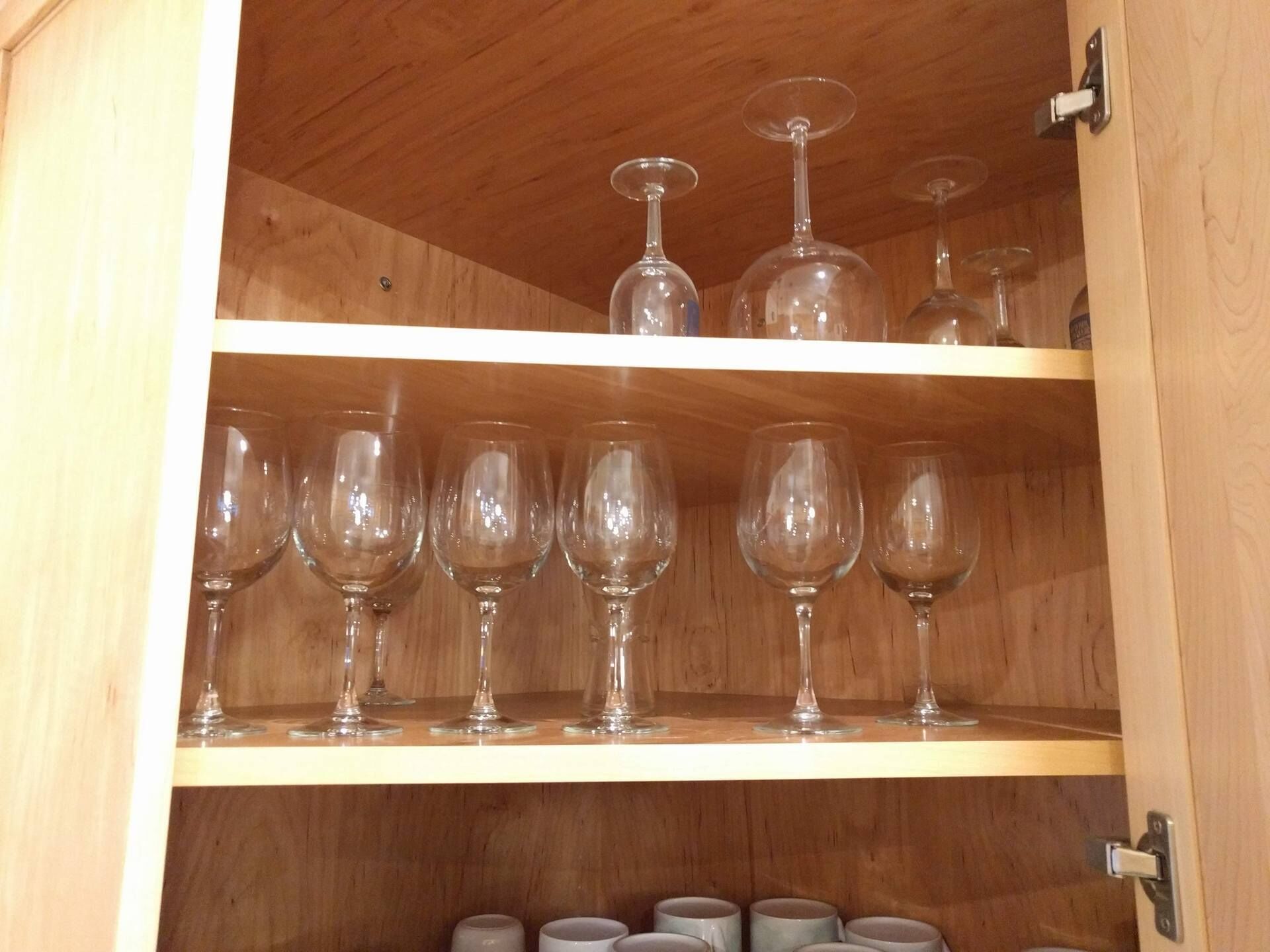 A wooden cabinet with two shelves, each holding multiple wine glasses.