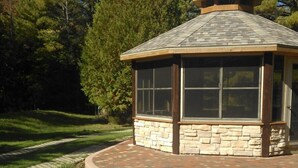 A stone and glass gazebo with a curved roof, surrounded by a brick pathway and greenery. - Perfect For Family Reunions/Weekend Getaways/Large Groups. A hidden oasis! (Fish Creek)